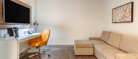 A modern room with a white desk, orange office chair, and a beige sectional sofa.