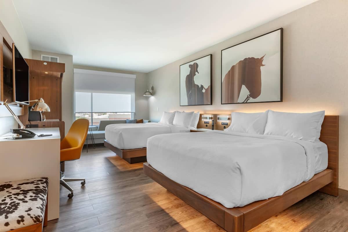A hotel room with two beds, a desk, a chair, and artwork on the wall.