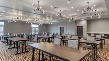 A conference room with multiple tables and chairs, ceiling lights, and a patterned carpet.