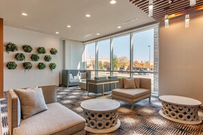 A modern lounge area with sofas, a coffee table, and a wall adorned with hexagonal planters. - Cambria Hotel Richardson - Dallas (Plano)