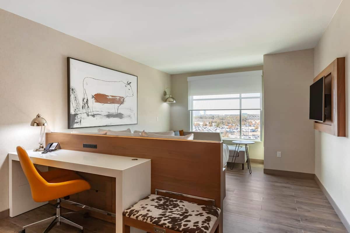 A modern office space with a desk, orange chair, and a large window offering a city view.