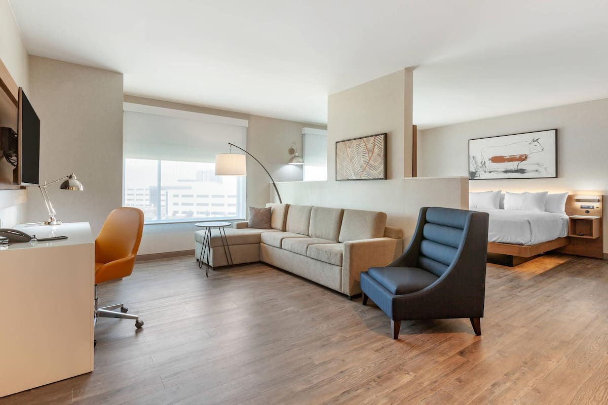 A modern hotel room with a sofa, armchair, desk, and a bed.