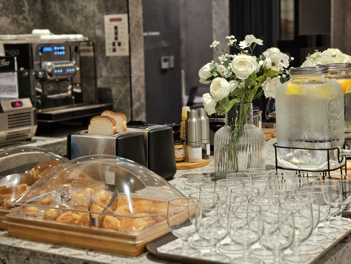 A buffet setup with pastries, a vase of flowers, and a large pitcher of iced tea.