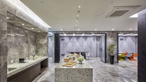 Una hall moderna di un hotel con una reception in marmo, un’area salotto con poltrone colorate e un’ampia pianta in vaso.