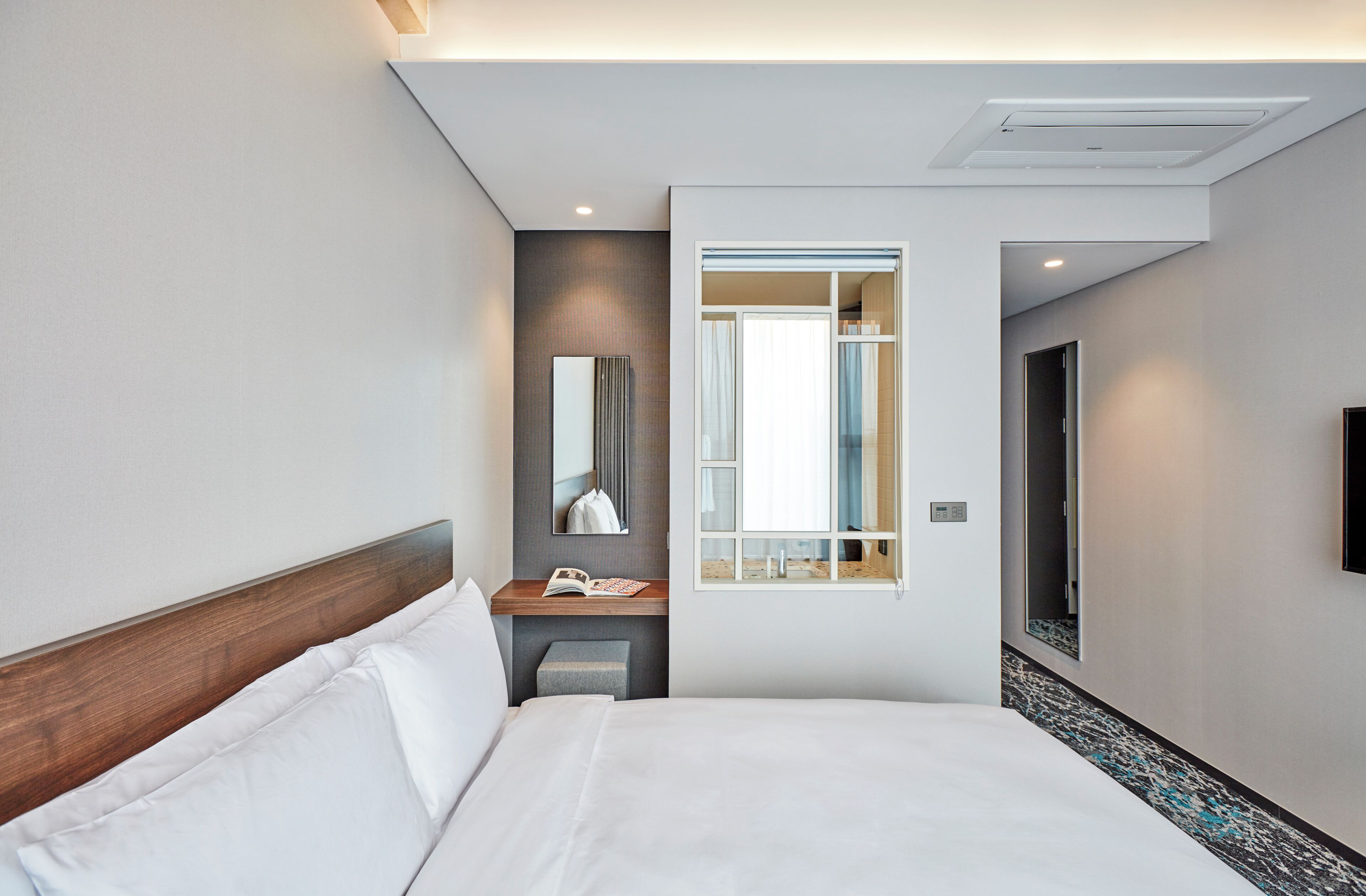 A modern hotel room with a large bed, a bedside table, a mirror, and a window with curtains.