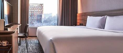 Una habitación de hotel con una cama grande, un escritorio con computadora, una silla y vistas a la ciudad desde la ventana.