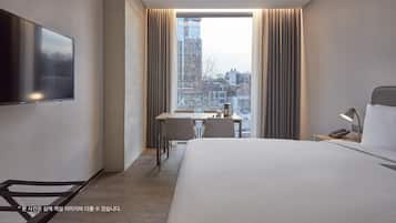 A modern hotel room with a large bed, a desk with a chair, a TV mounted on the wall, and a window with curtains.