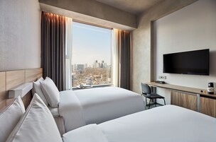 Habitación de hotel con dos camas, un escritorio, una silla, un televisor y vistas a la ciudad.