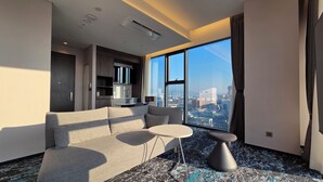 Una moderna camera d'hotel con una grande finestra che offre vista sulla città, un divano, un piccolo tavolo rotondo e un angolo cottura.