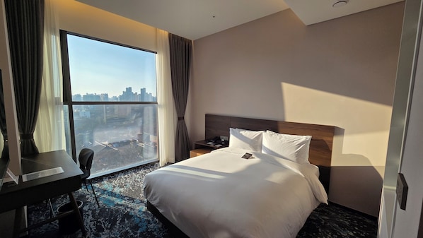 Una habitación de hotel con un ventanal grande, una cama, un escritorio y una silla.