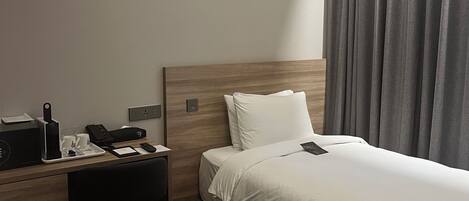 A hotel room with a bed, a desk, a chair, a telephone, and a small table with cups and a knife.
