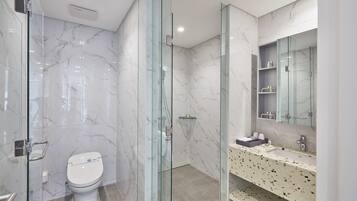 Une salle de bain moderne avec une douche à parois de verre, un mur recouvert de carreaux de marbre, des toilettes blanches et un plan de toilette avec un lavabo et un miroir.