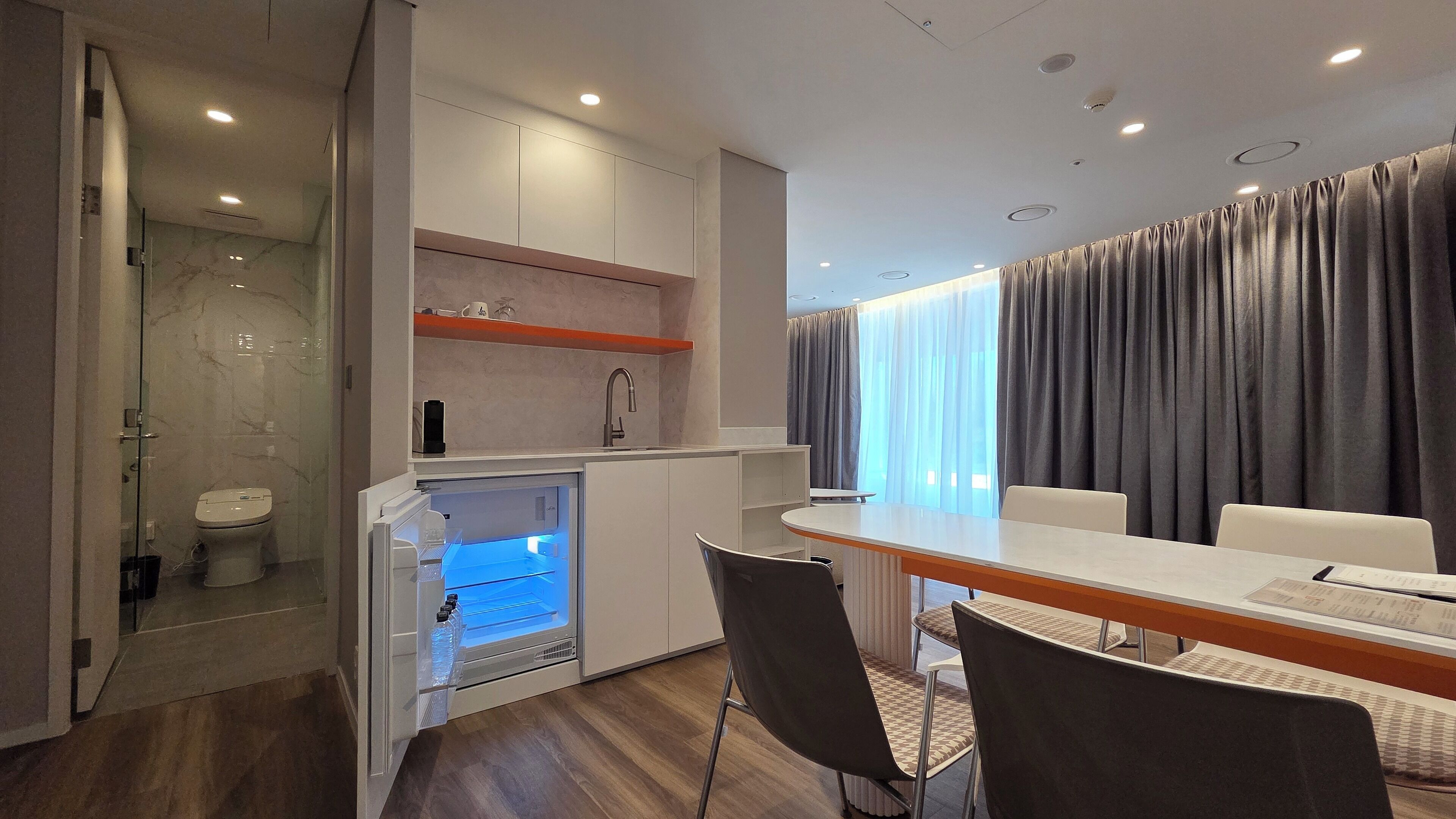 A compact hotel room with a kitchenette, a dining area, and a shower.