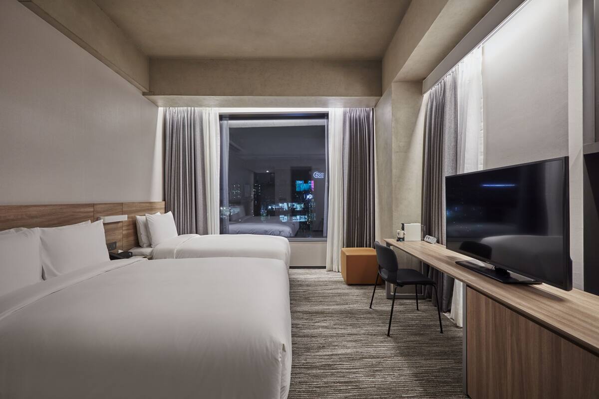 Ett hotellrum med två sängar, en TV, ett skrivbord och ett fönster med gardiner.