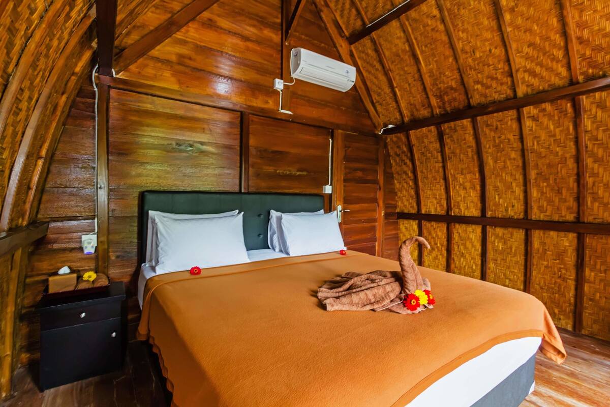 Una habitación acogedora con techo de madera, una cama con almohadas blancas, una manta marrón y una toalla con flores.