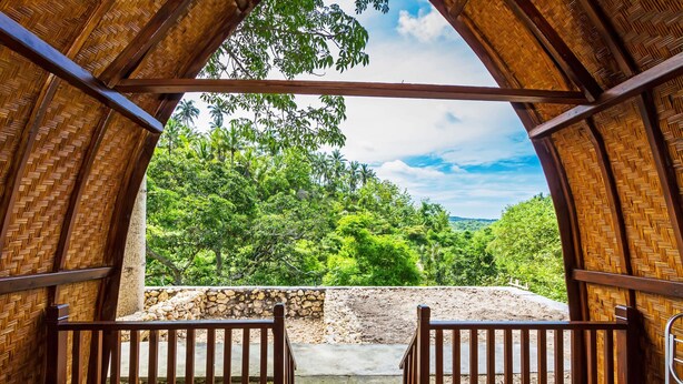 A wooden deck with a view of lush greenery and a stone wall. - Butterfly Bungalows (Penida Island)