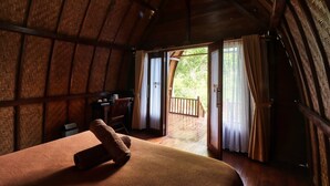 A rustic wooden room with a bed, a desk, and a view of the outdoors. - Butterfly Bungalows (Penida Island)