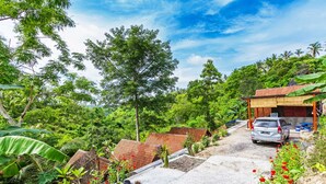 A residential area with a paved driveway leading to a house with a red-tiled roof. - Butterfly Bungalows (Penida Island)