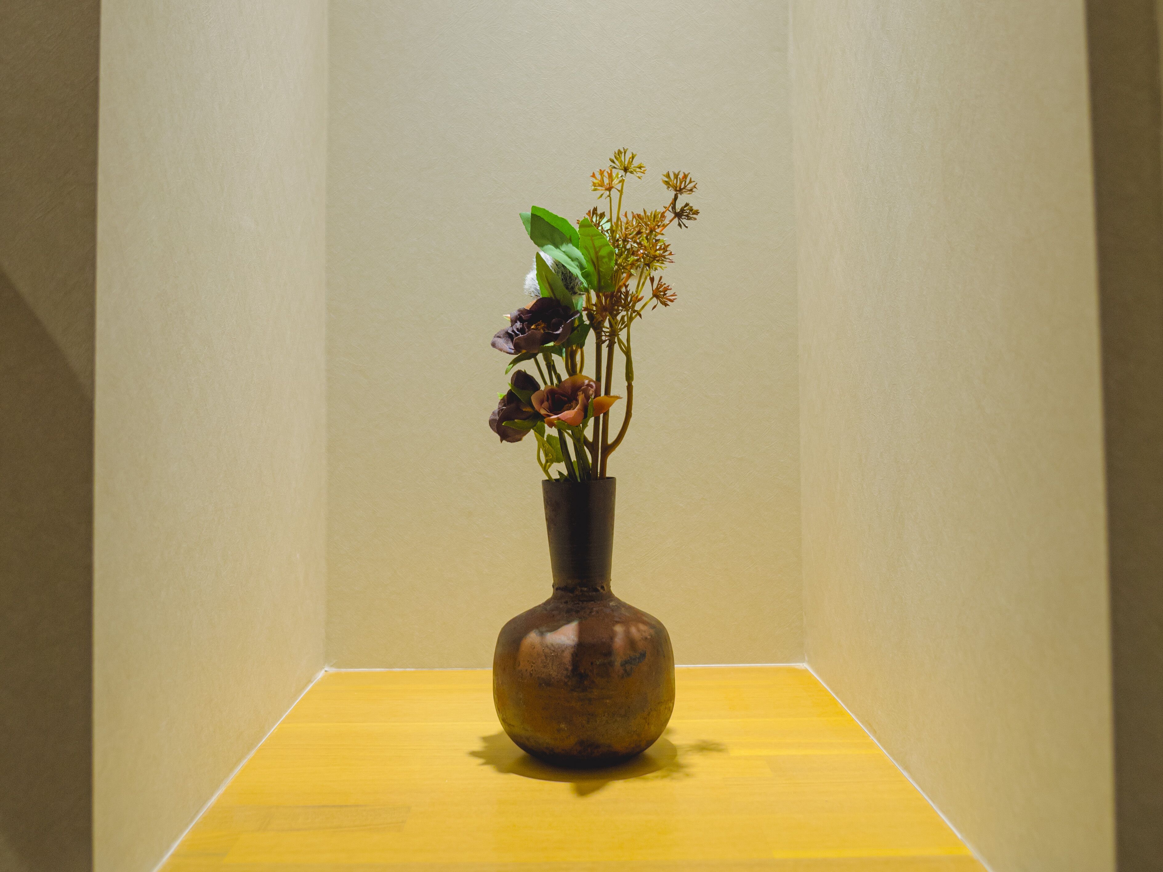 Un vase rempli de fleurs est posé sur une table jaune, devant un mur de couleur beige.