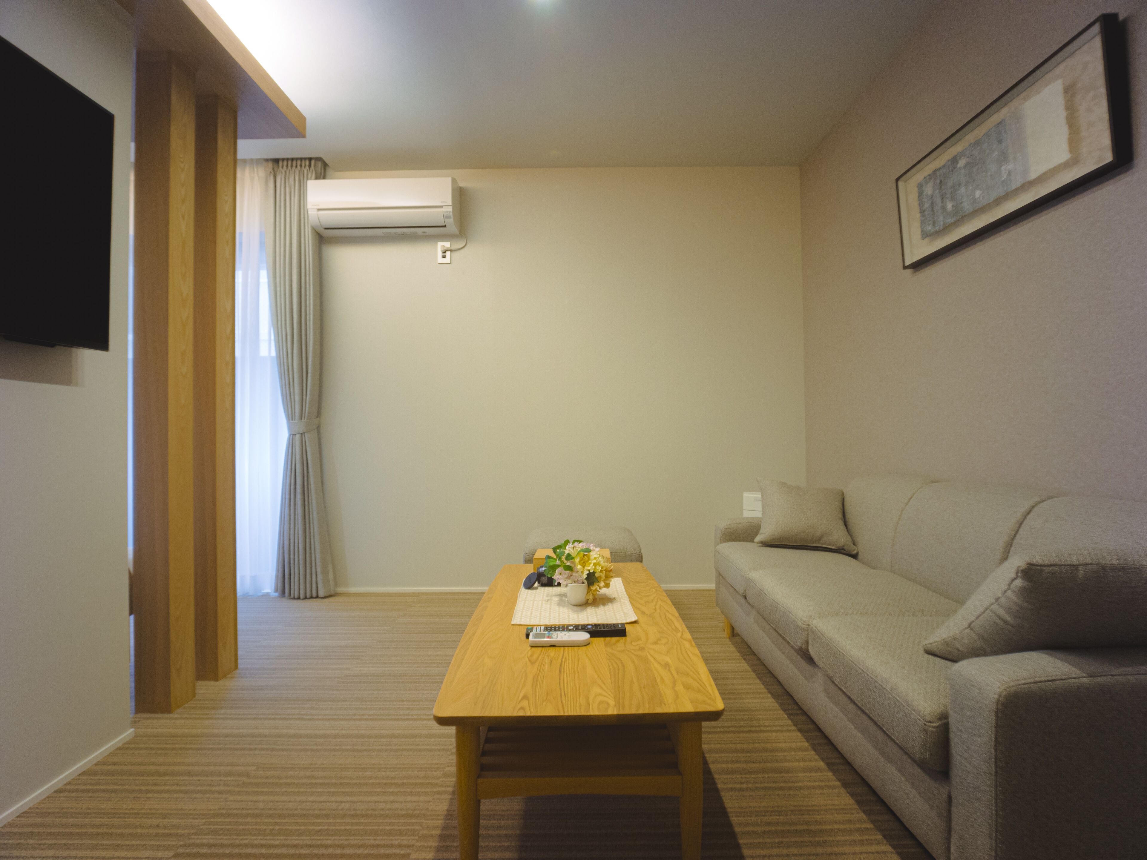 A living room with a wooden coffee table, beige sofa, and a mounted TV.