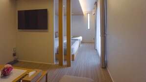 Ein Hotelzimmer mit einem Bett, einem Schreibtisch mit Fernbedienung, einem an der Wand befestigten Fernseher und einem Fenster, das natürliches Licht hereinlässt.