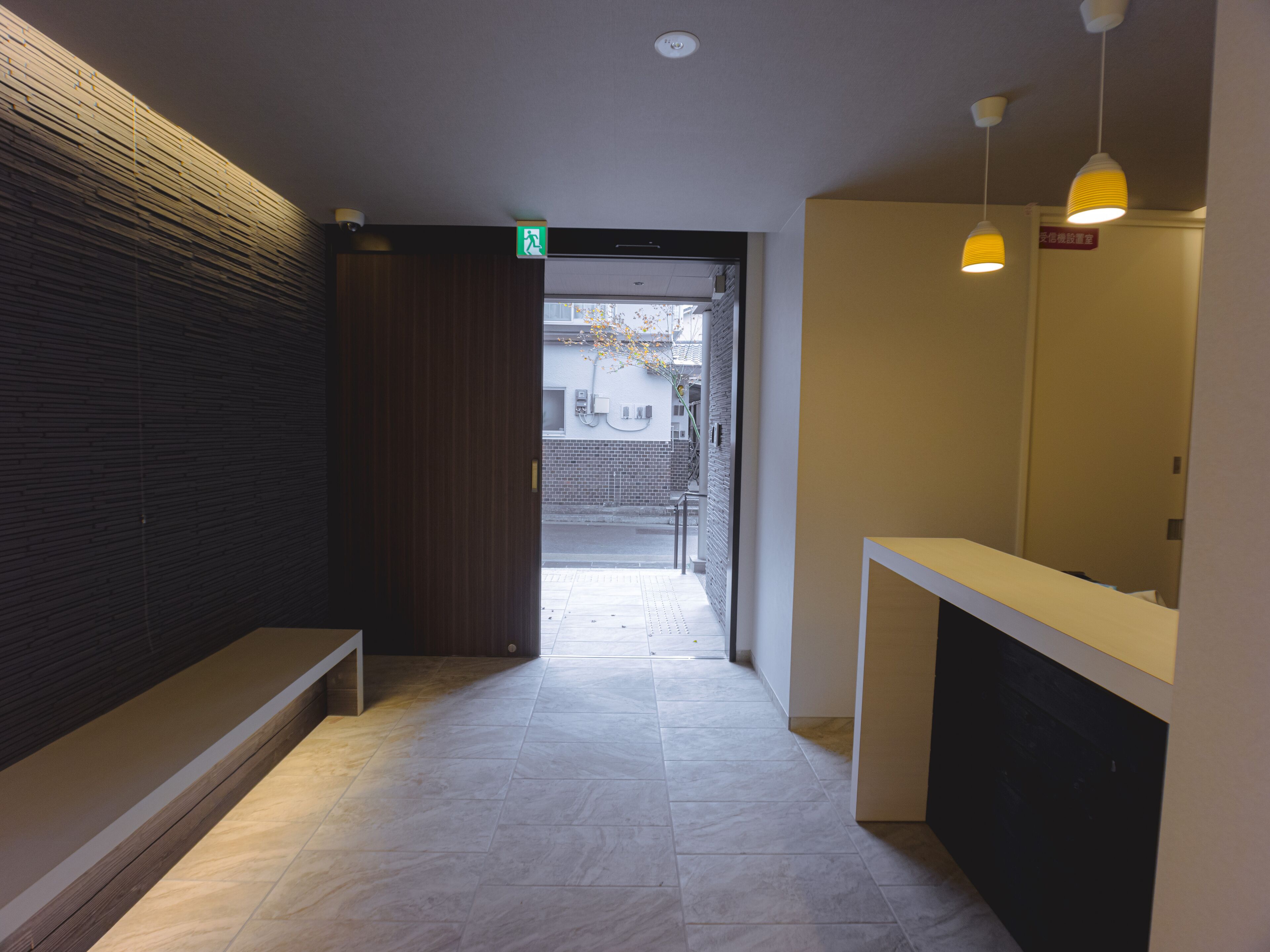 A hallway with a bench, a reception desk, and a door leading outside.