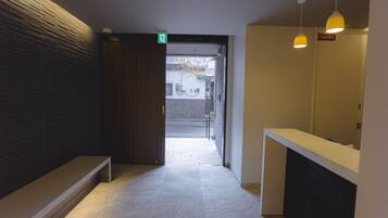 A hallway with a bench, a reception desk, and a door leading outside.