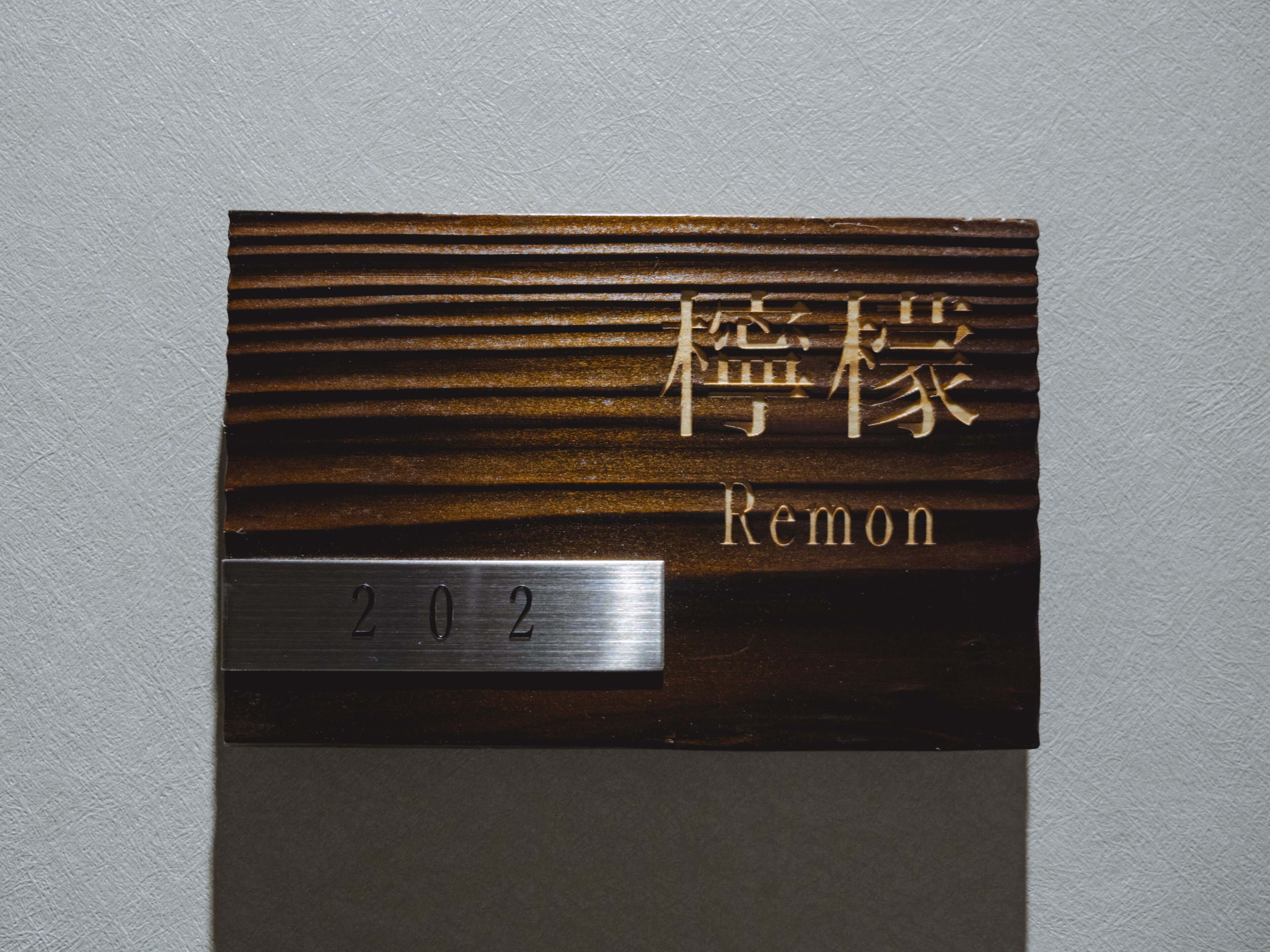 A room number plaque with the number 202 and the name "Remon" on a textured wall.