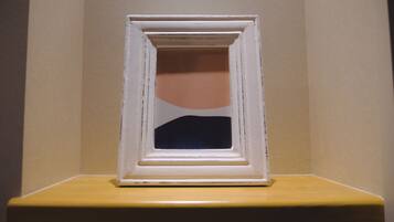 Un tableau encadré, dont le centre est plus foncé, est posé sur une étagère, adossé à un mur.