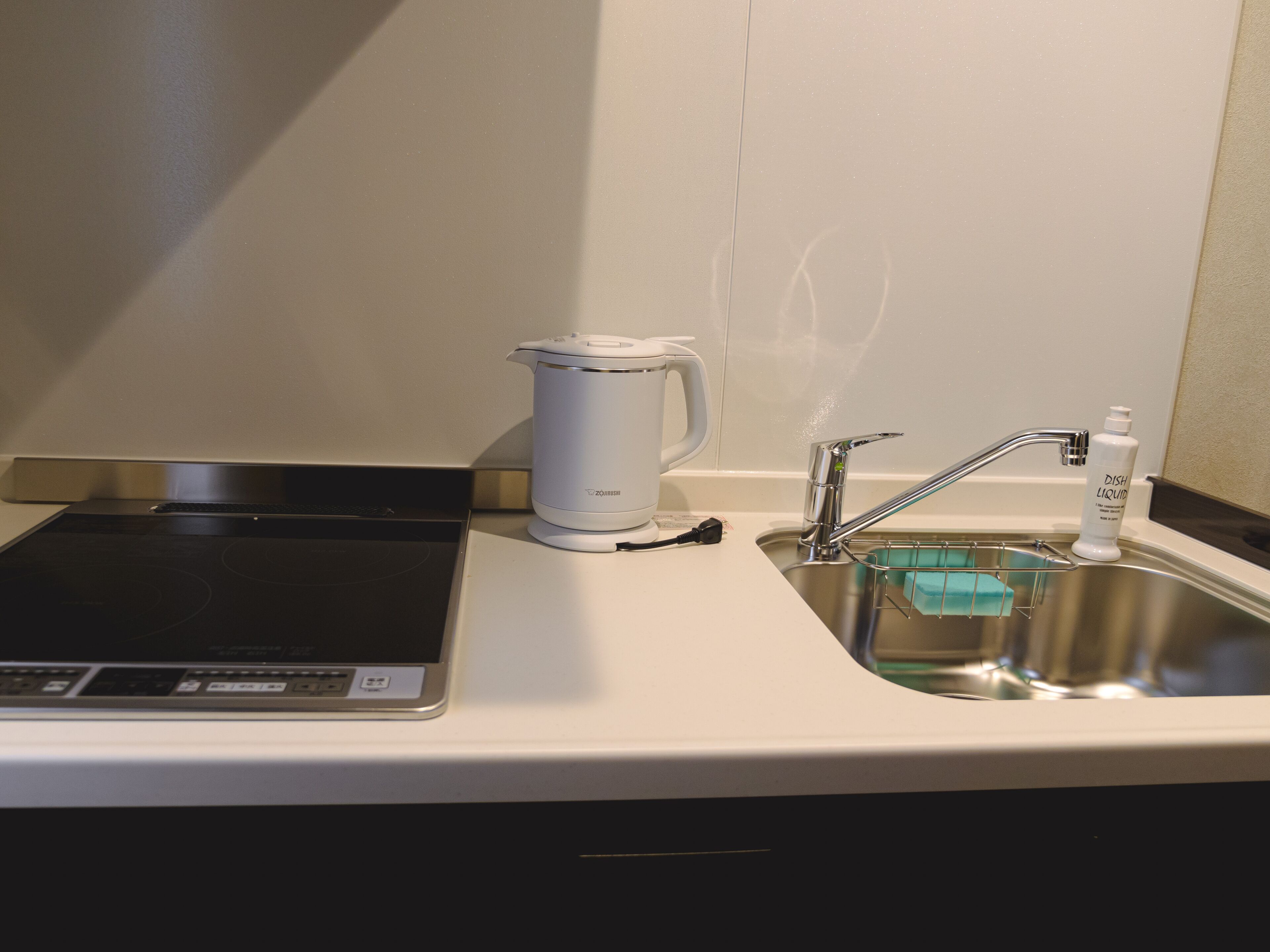 A kitchen with a built-in induction cooktop, a kettle, a sink with a dish soap bottle, and a faucet.