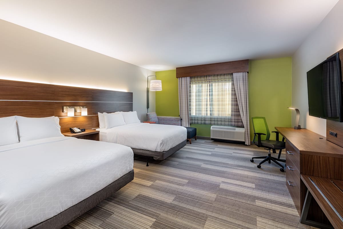 Habitación de hotel con dos camas, un escritorio, una silla, un televisor y una ventana con cortinas.
