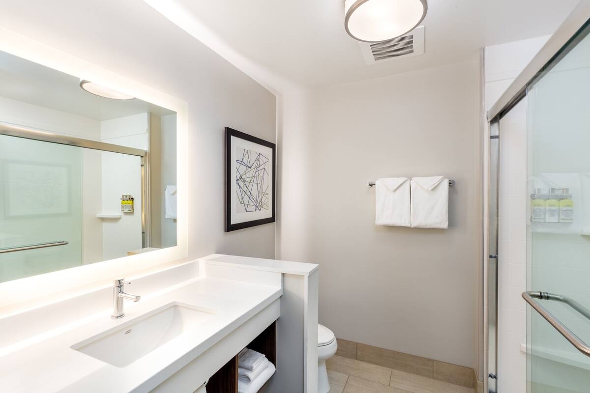 Un baño moderno con un espejo grande, lavabo blanco y cabina de ducha de vidrio.
