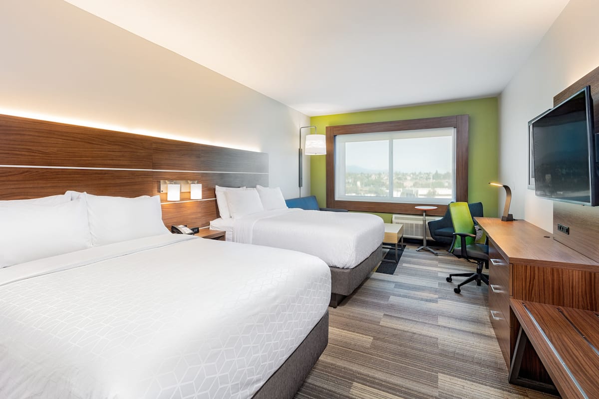 Habitación de hotel con dos camas, un escritorio, una silla, un televisor y una ventana con vistas.