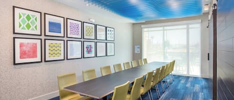 A conference room with a long table and chairs, framed artwork on the wall, and a large window.