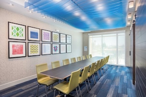 A conference room with a long table and chairs, framed artwork on the wall, and a large window.