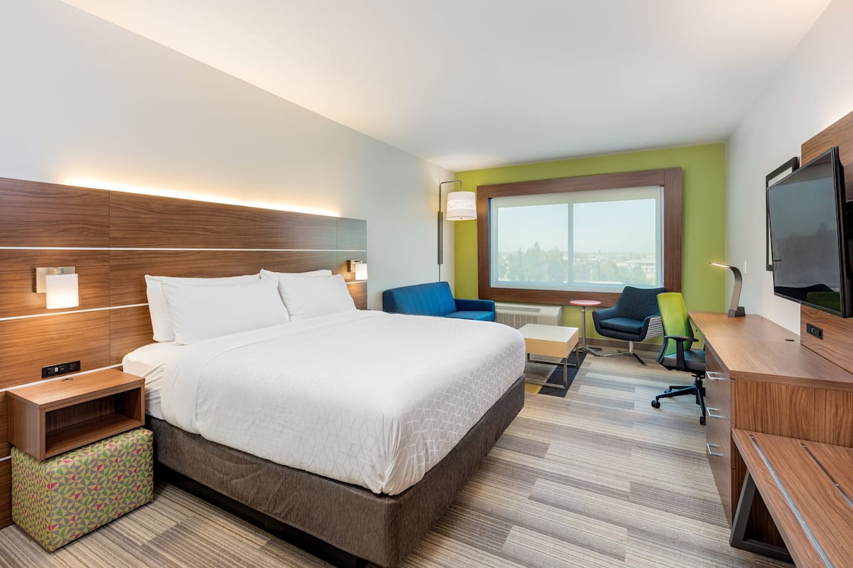 Una habitación de hotel moderna con una cama grande, un escritorio, una silla y un televisor.