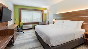 A modern hotel room with a large bed, a desk with a chair, a television, and a window with a city view.