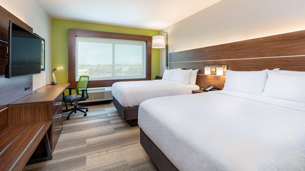 A hotel room with two beds, a desk, a chair, a TV, and a large window with a city view.