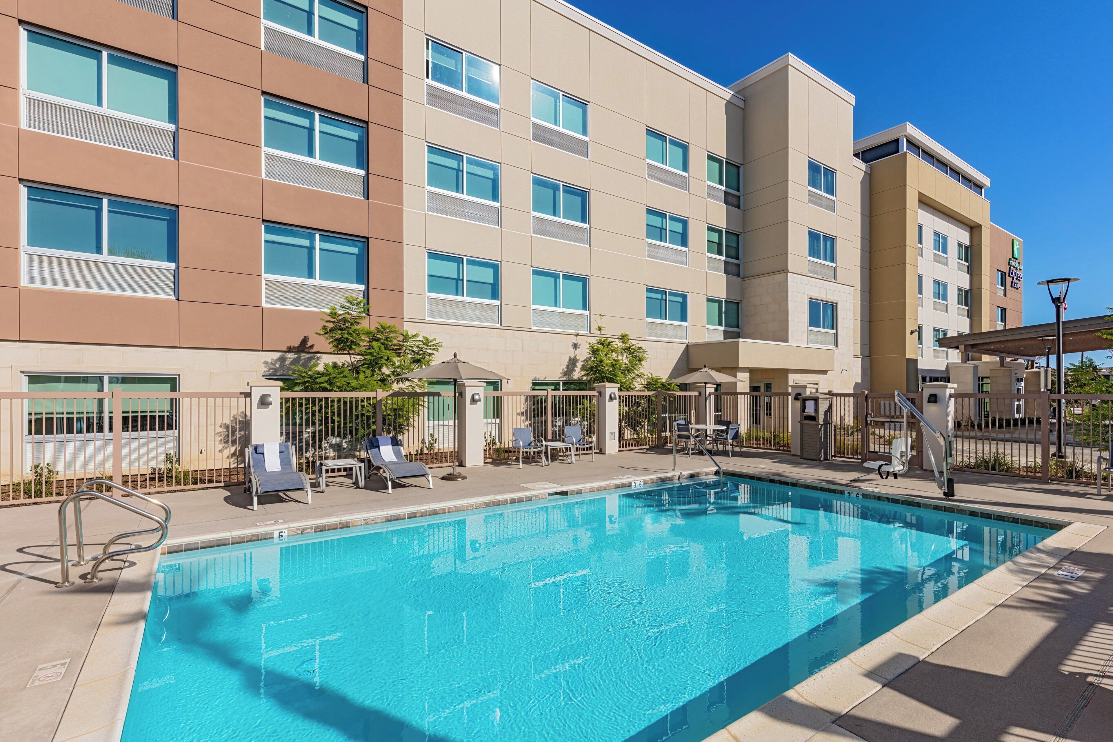Un hotel con piscina, mobiliario exterior y un cielo azul despejado.