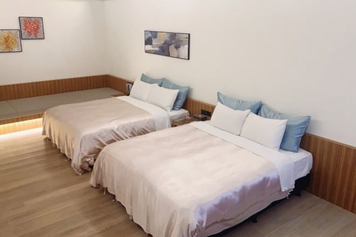 Une chambre avec deux lits, chacun équipé d’un oreiller et d’une couverture, ainsi que d’une table de chevet et d’un tableau accroché au mur.