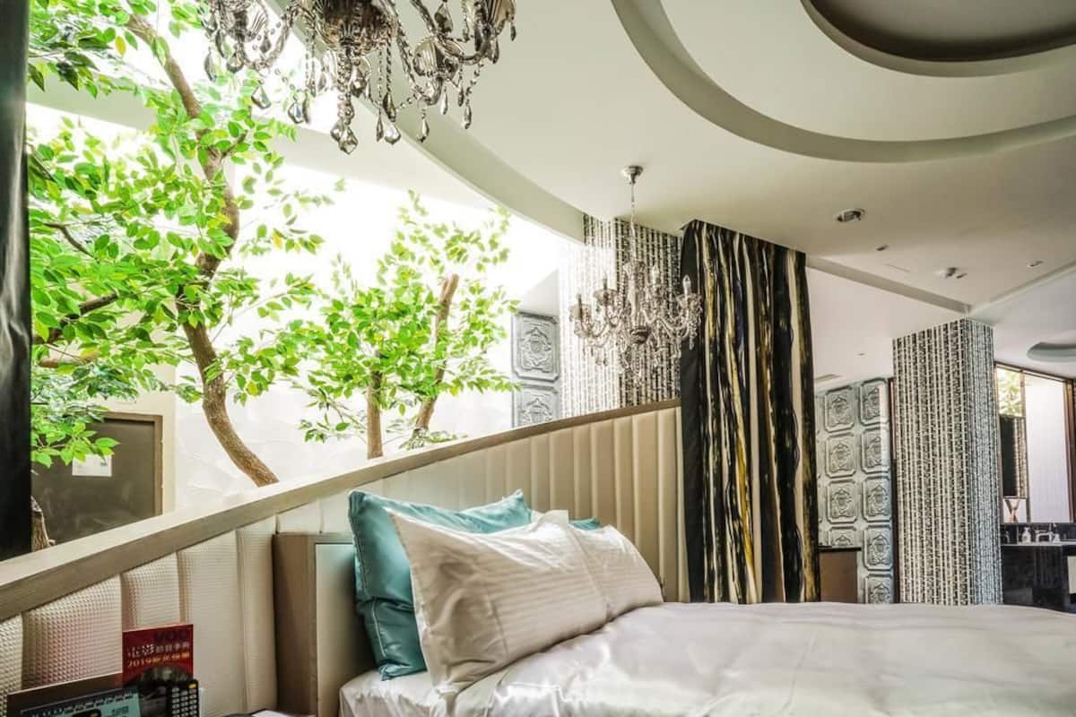 A modern hotel room with a bed, a telephone, and a view of trees through a window.