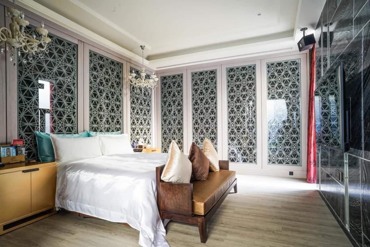 A bedroom with a bed, a wooden bench with cushions, a nightstand, and a decorative wall panel.