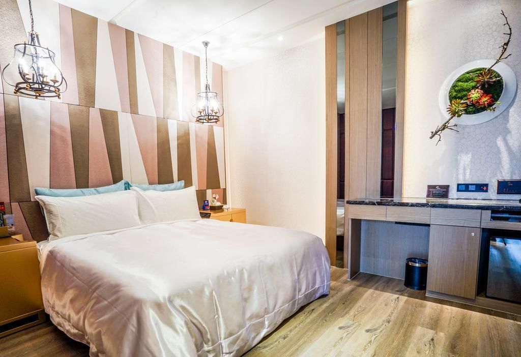 Een moderne hotelkamer met een groot bed, een houten hoofdbord, een ingebouwde bureau met een magnetron en een kleine prullenbak.