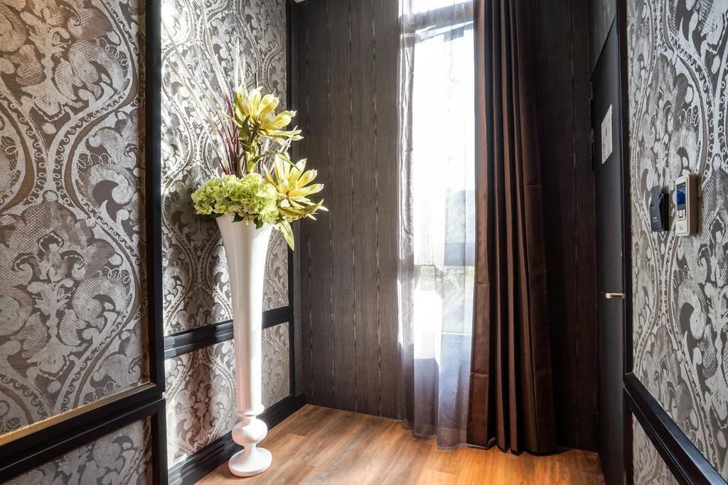 A hallway with patterned wallpaper, a white vase with flowers, and a wooden floor.