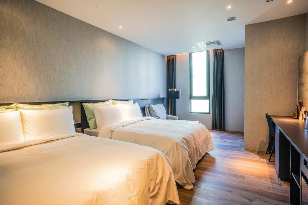 A hotel room with two beds, a desk, and a large window with curtains.