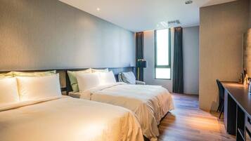 A hotel room with two beds, a desk, and a large window with curtains.
