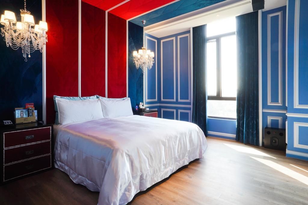 Ein Schlafzimmer mit einem großen Bett, zwei Nachttischen, einer Chandelüster und einem fenster mit Vorhängen.