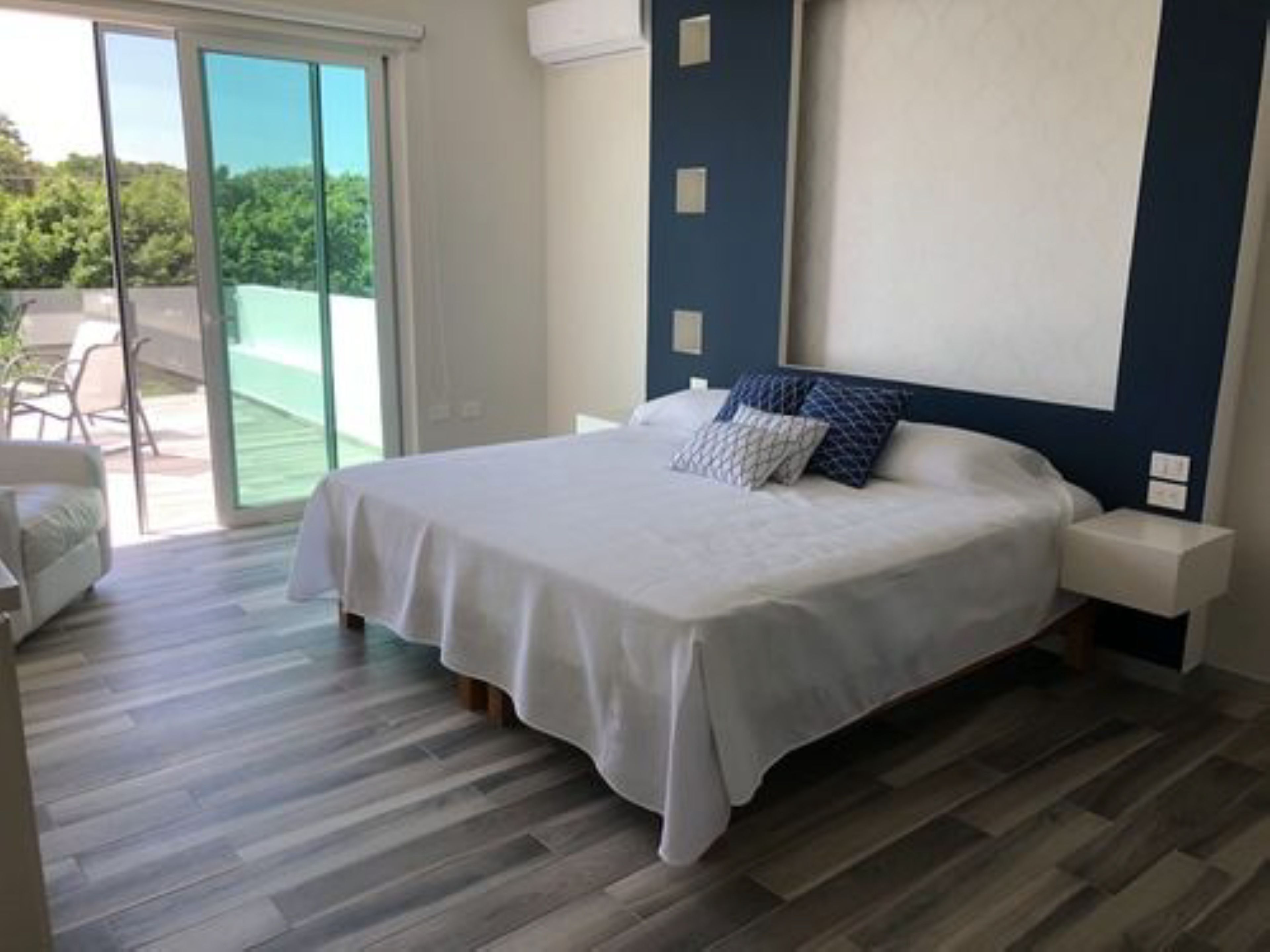 Ein Schlafzimmer mit einem Bett, einem Nachttisch und Blick auf eine Terrasse mit einem Stuhl.