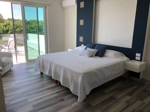 A bedroom with a bed, a nightstand, and a view of a patio with a chair.