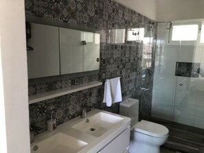 A modern bathroom with a double sink, toilet, and a glass shower enclosure.